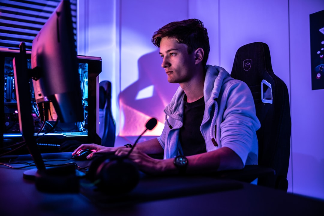 A gamer focused on their screen, with a dynamic gaming setup featuring a computer, headset, and colorful LED lights.